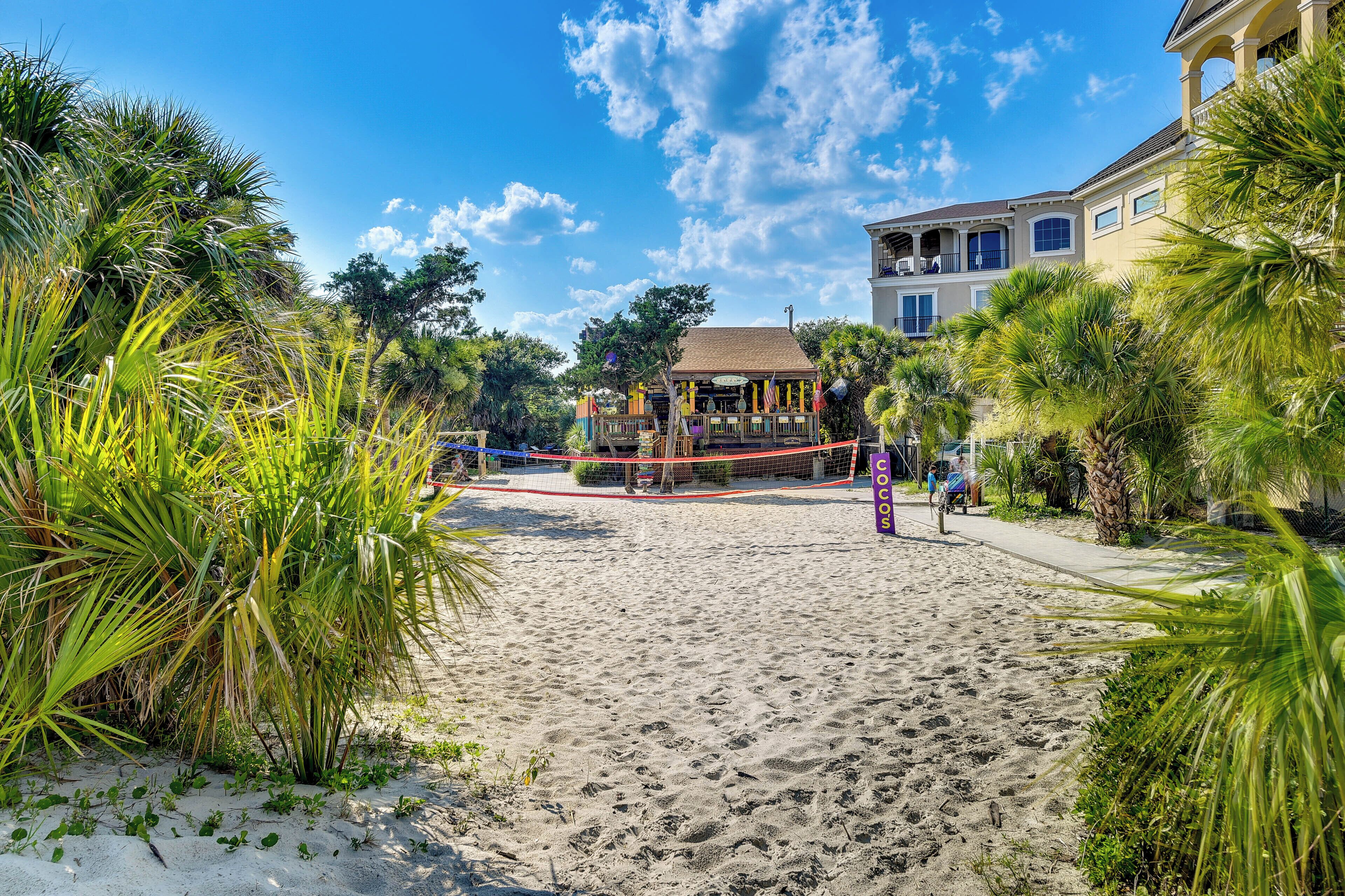 A beach with a volleyball net, palm trees, and a building with balconies.