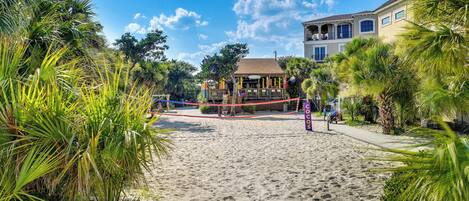 A beach with a volleyball net, palm trees, and a building with balconies.