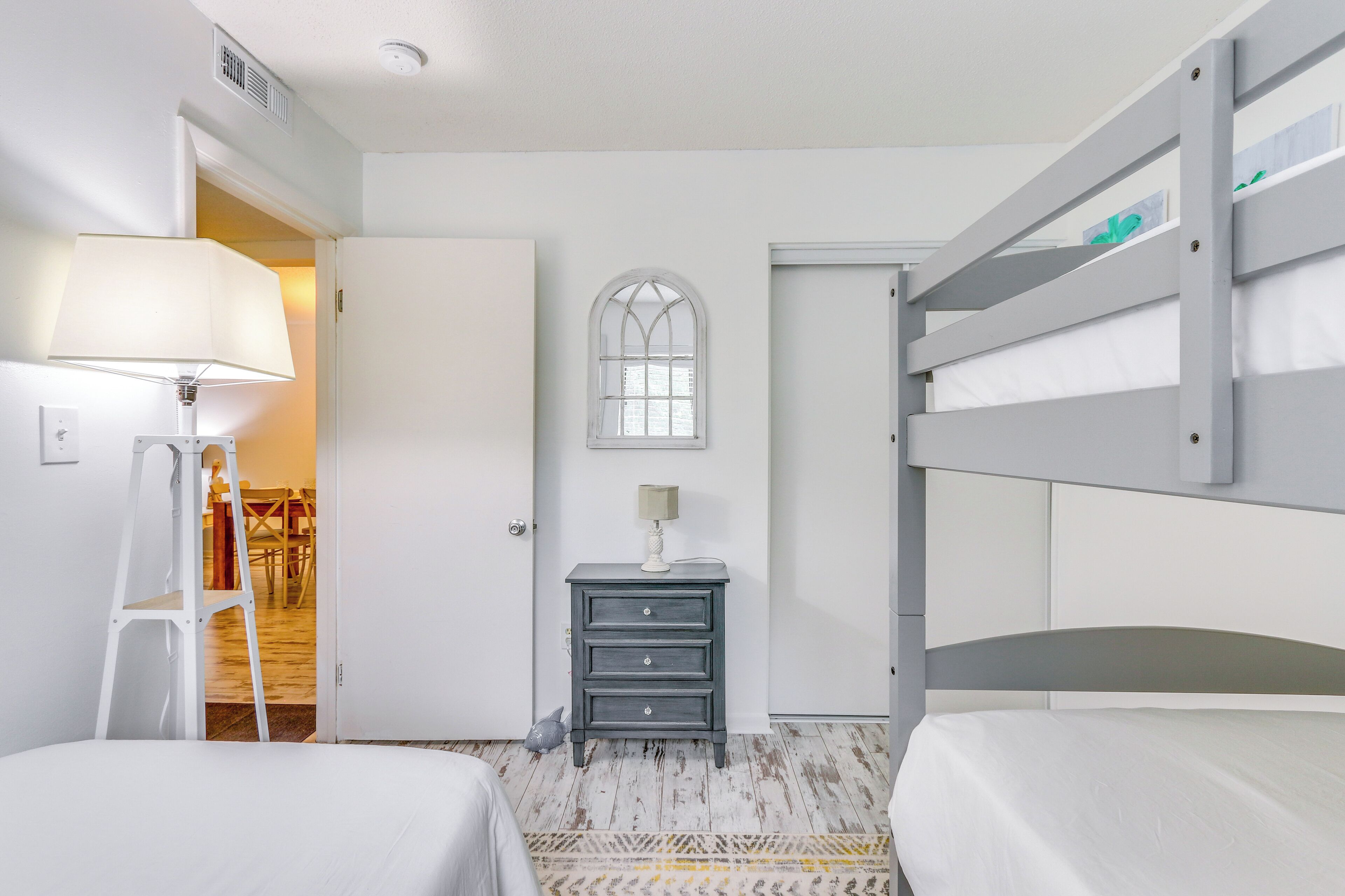 A bedroom with two beds, a dresser, a lamp, a window, and a door.