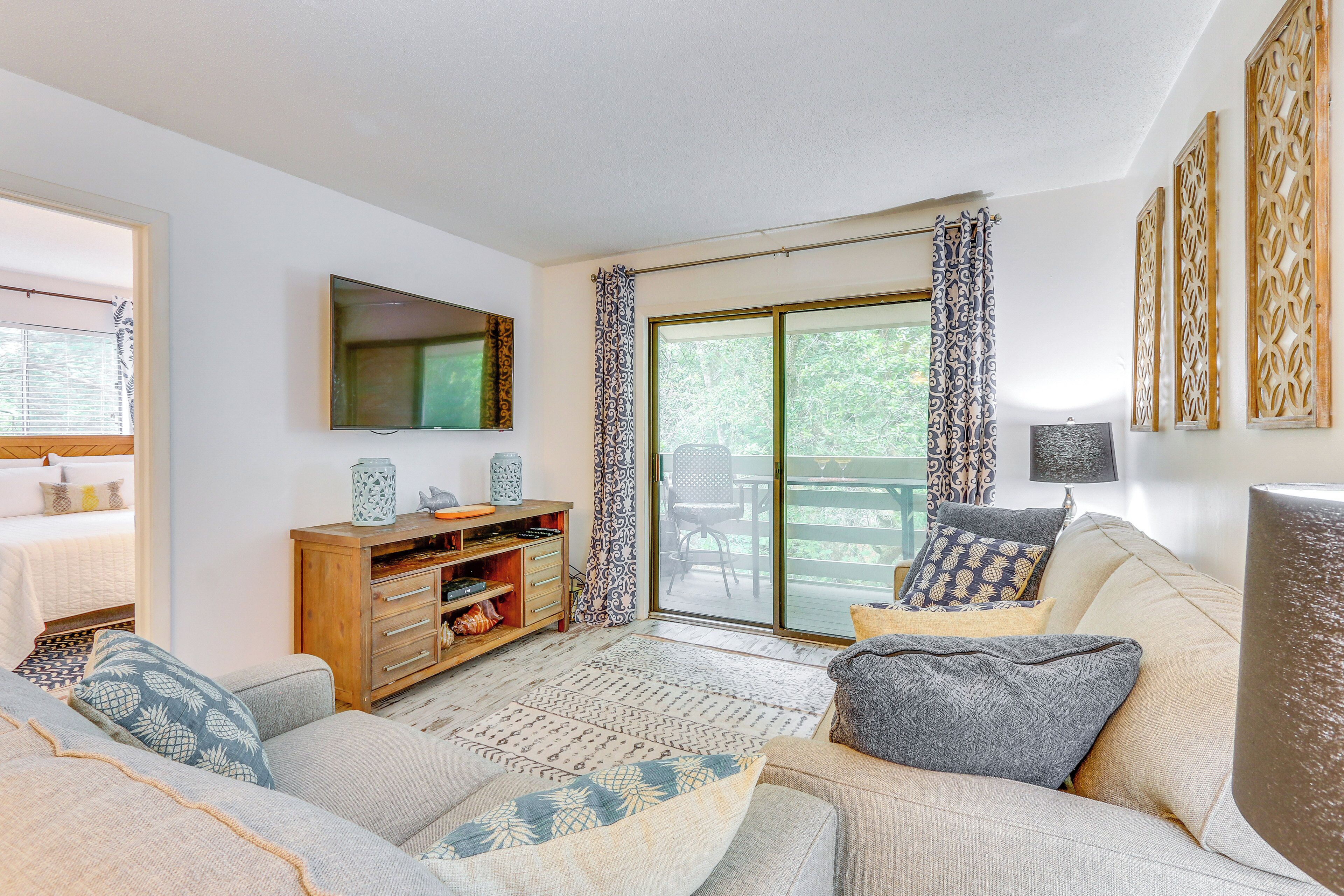 A living room with a sofa, a wooden cabinet, a flat-screen TV, and a sliding glass door leading to an outdoor area.