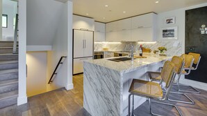 A modern kitchen with a marble island, stainless steel appliances, and wicker bar stools. - Deer Valley Retreat w/ Hot Tub & Movie Room (Park City)