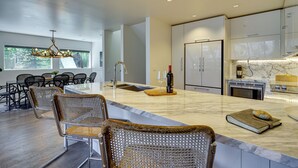 A modern kitchen with a large island, stainless steel appliances, and a dining area with wicker chairs. - Deer Valley Retreat w/ Hot Tub & Movie Room (Park City)