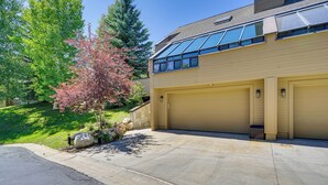 A two-story house with a garage, a tree with pink leaves, and a clear sky. - Deer Valley Retreat w/ Hot Tub & Movie Room (Park City)