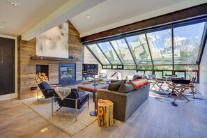 A spacious living room with a fireplace, comfortable seating, and large windows offering a view of the outdoors. - Deer Valley Retreat w/ Hot Tub & Movie Room (Park City)