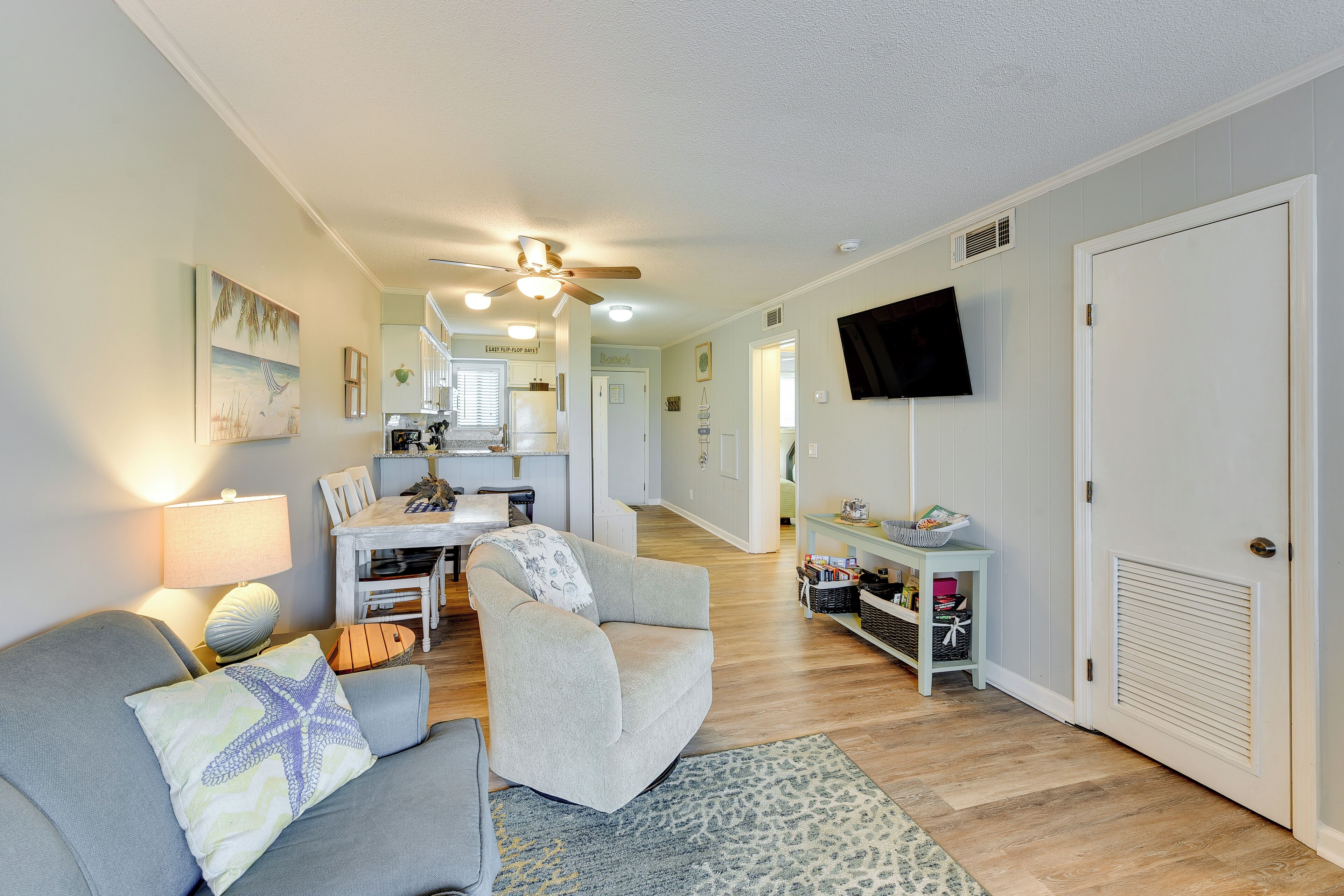 A living room with a sofa, armchair, and a TV mounted on the wall.