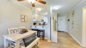 A dining area with a wooden table and bench, a ceiling fan, and a kitchen in the background. - < 1 Mi to Beach: Hilton Head Island Condo w/ Pool! (Hilton Head Island)