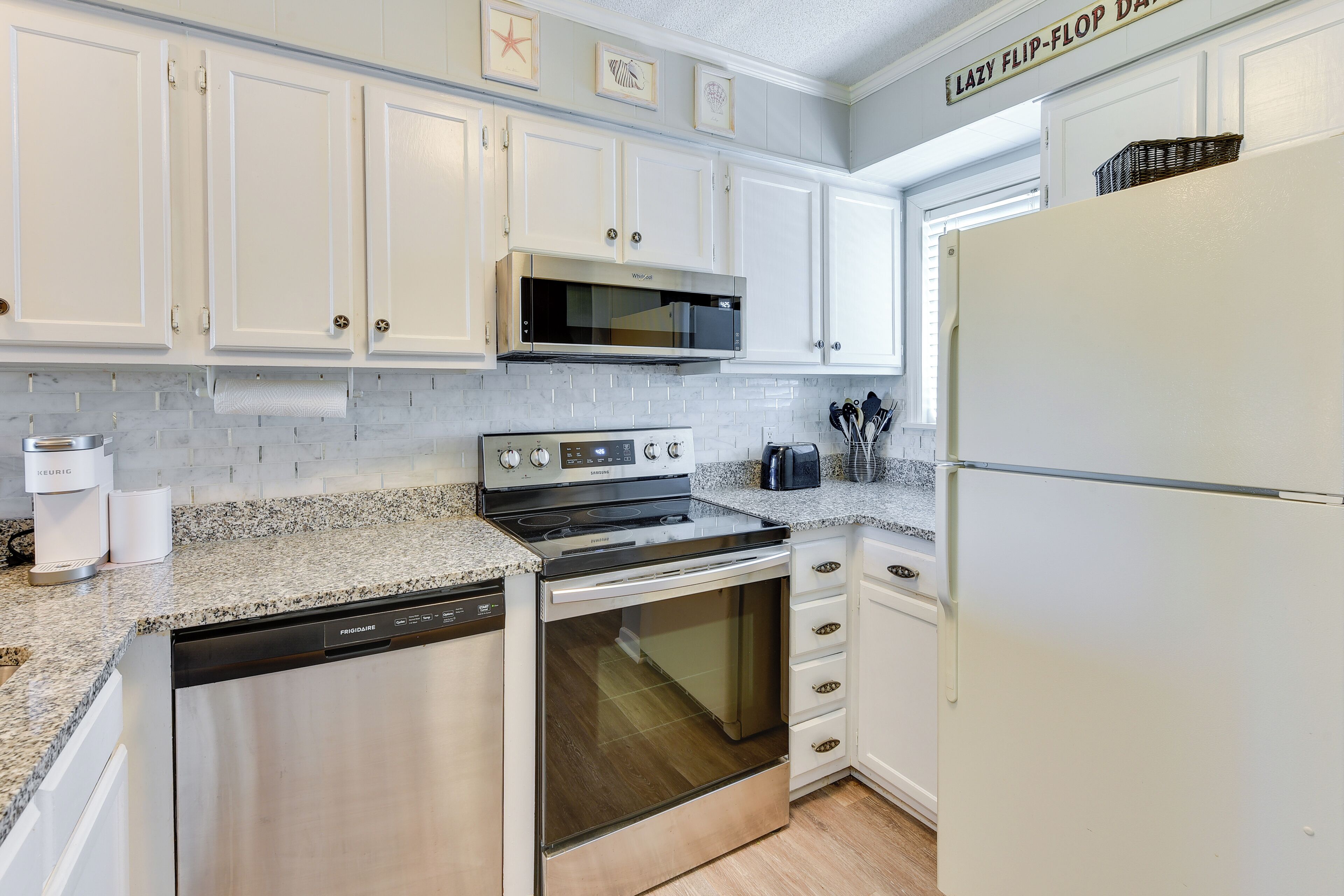 A kitchen with white cabinets, a stainless steel dishwasher, a microwave, a stove, and a refrigerator.