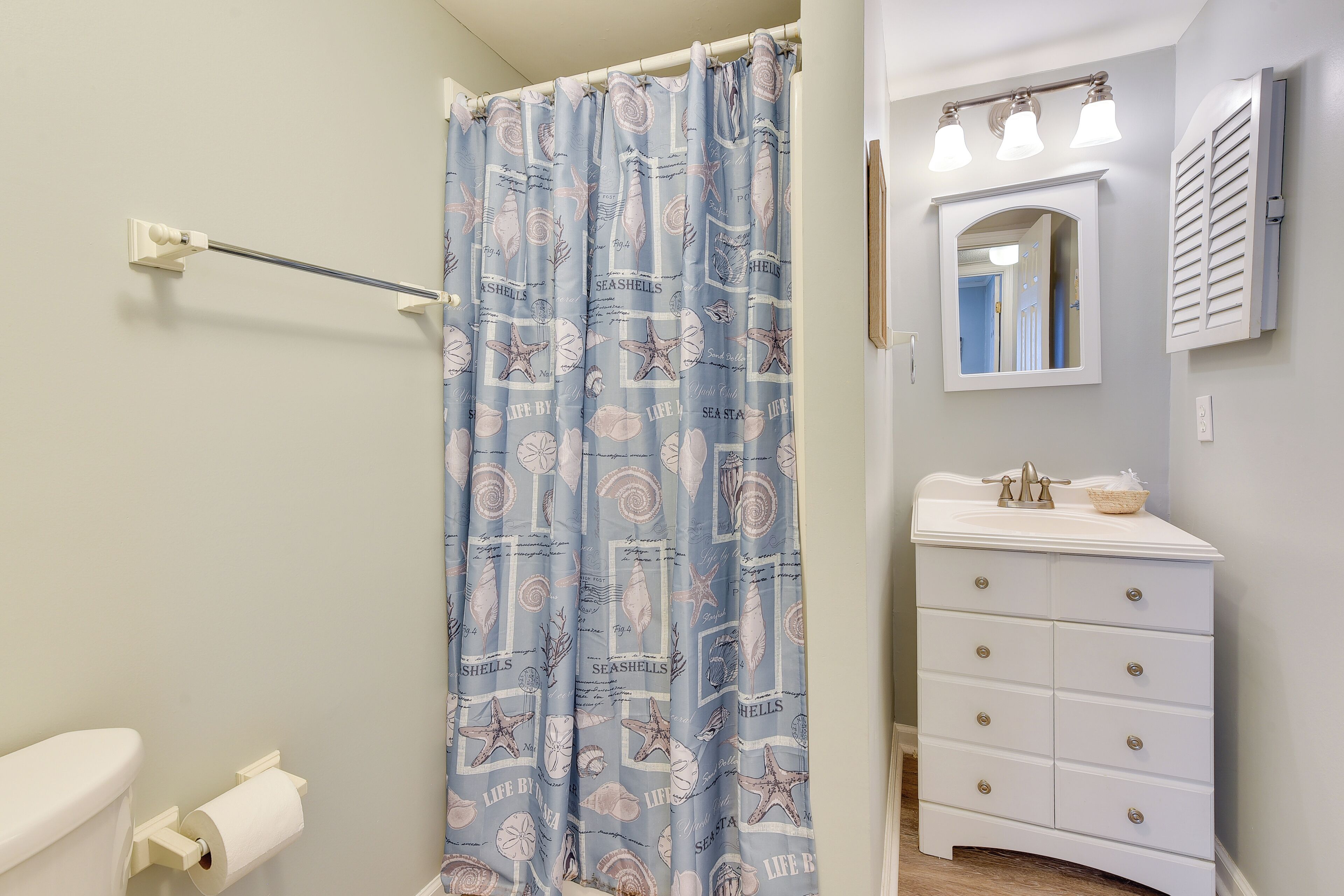Une salle de bain équipée d’un rideau de douche, de toilettes, d’un meuble-lavabo avec un miroir et d’un luminaire.