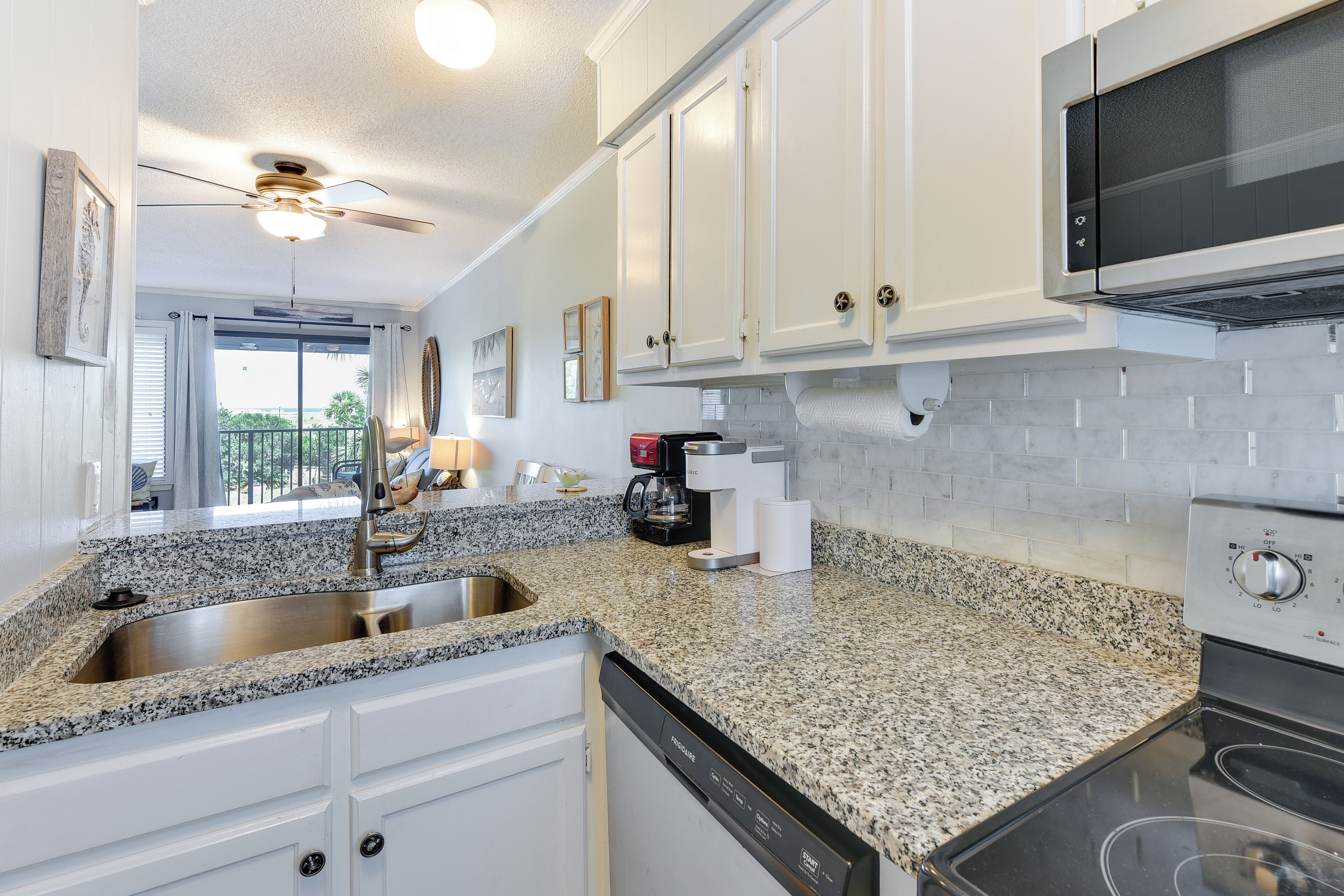 A kitchen with white cabinets, granite countertops, a stainless steel sink, a dishwasher, a microwave, and a stove.