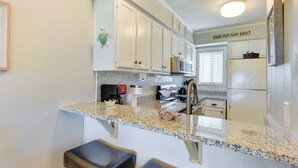 A kitchen with white cabinets, a granite countertop, and a sign that reads "LAZY FLIP-FLOP DAYS". - < 1 Mi to Beach: Hilton Head Island Condo w/ Pool! (Hilton Head Island)