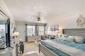 Une chambre à coucher comprenant un lit, des tables de chevet, un bureau, une chaise, un ventilateur de plafond et une grande fenêtre.