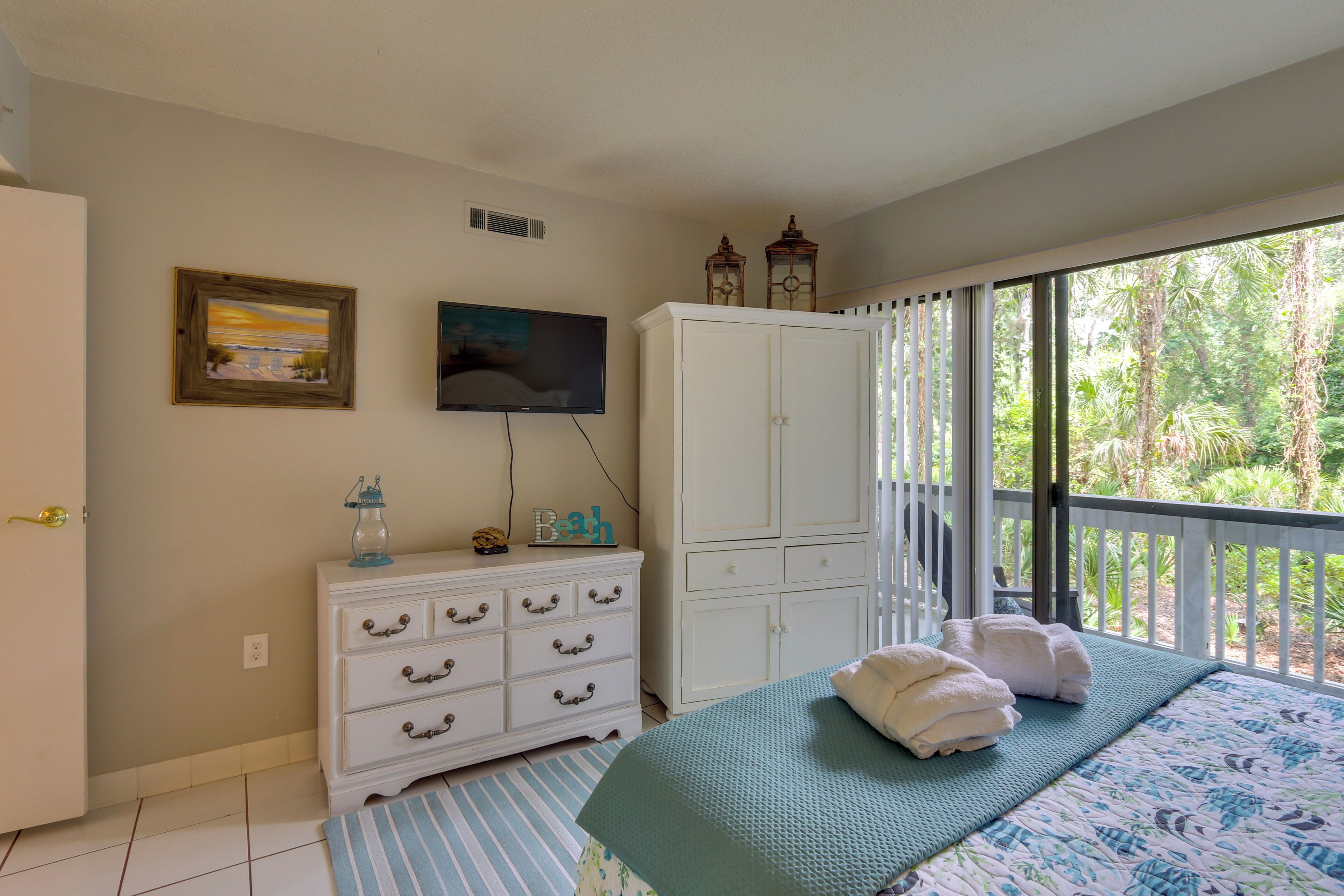 Une chambre à coucher comprenant un lit, une commode, un téléviseur et une fenêtre donnant sur un paysage verdoyant.