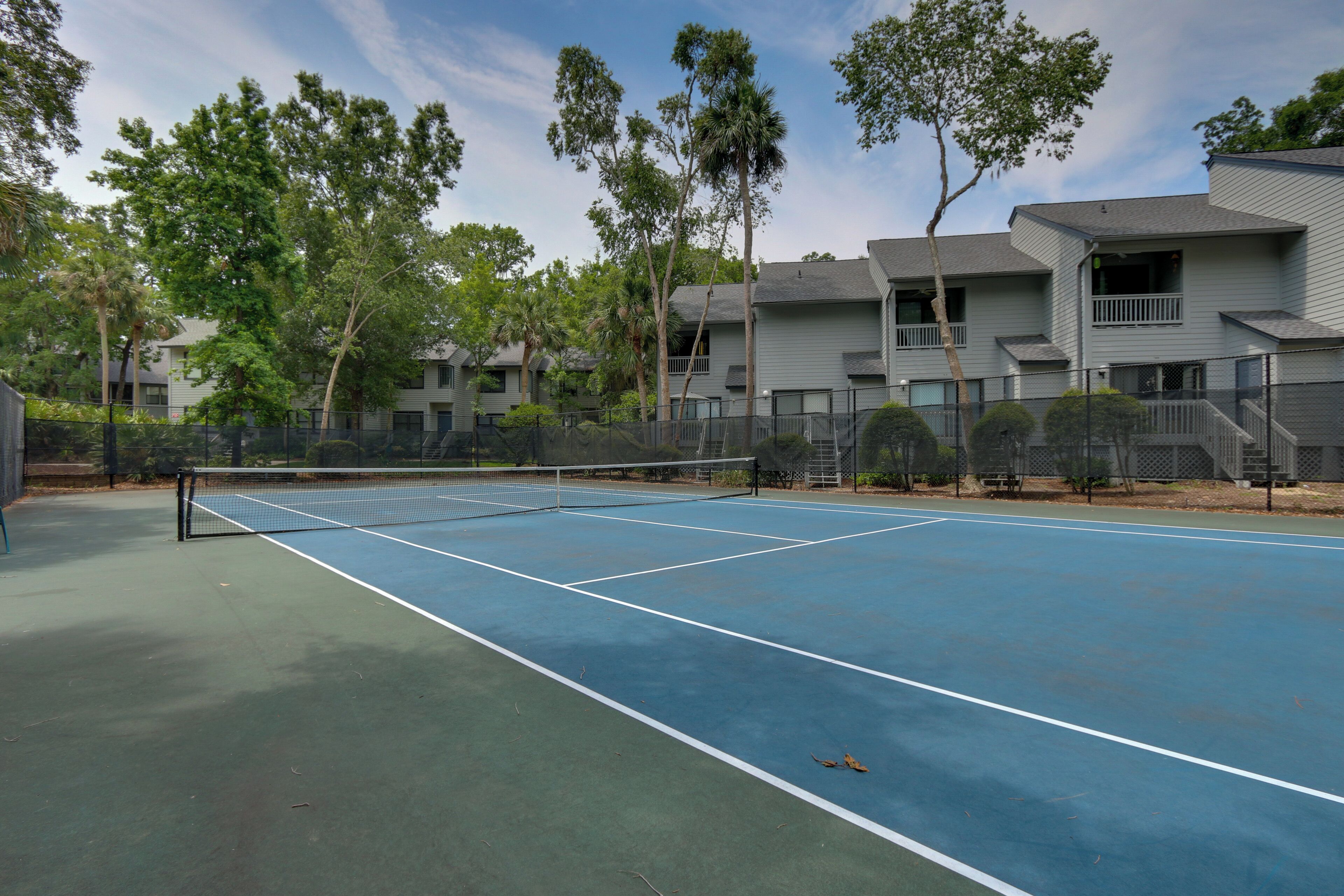 Un court de tennis en plein air, entouré d’arbres et d’immeubles d’habitation.