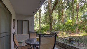An outdoor patio with a round table and chairs, surrounded by a lush garden and tall trees. - Serene Hilton Head Island Condo w/ Community Pool! (Hilton Head Island)