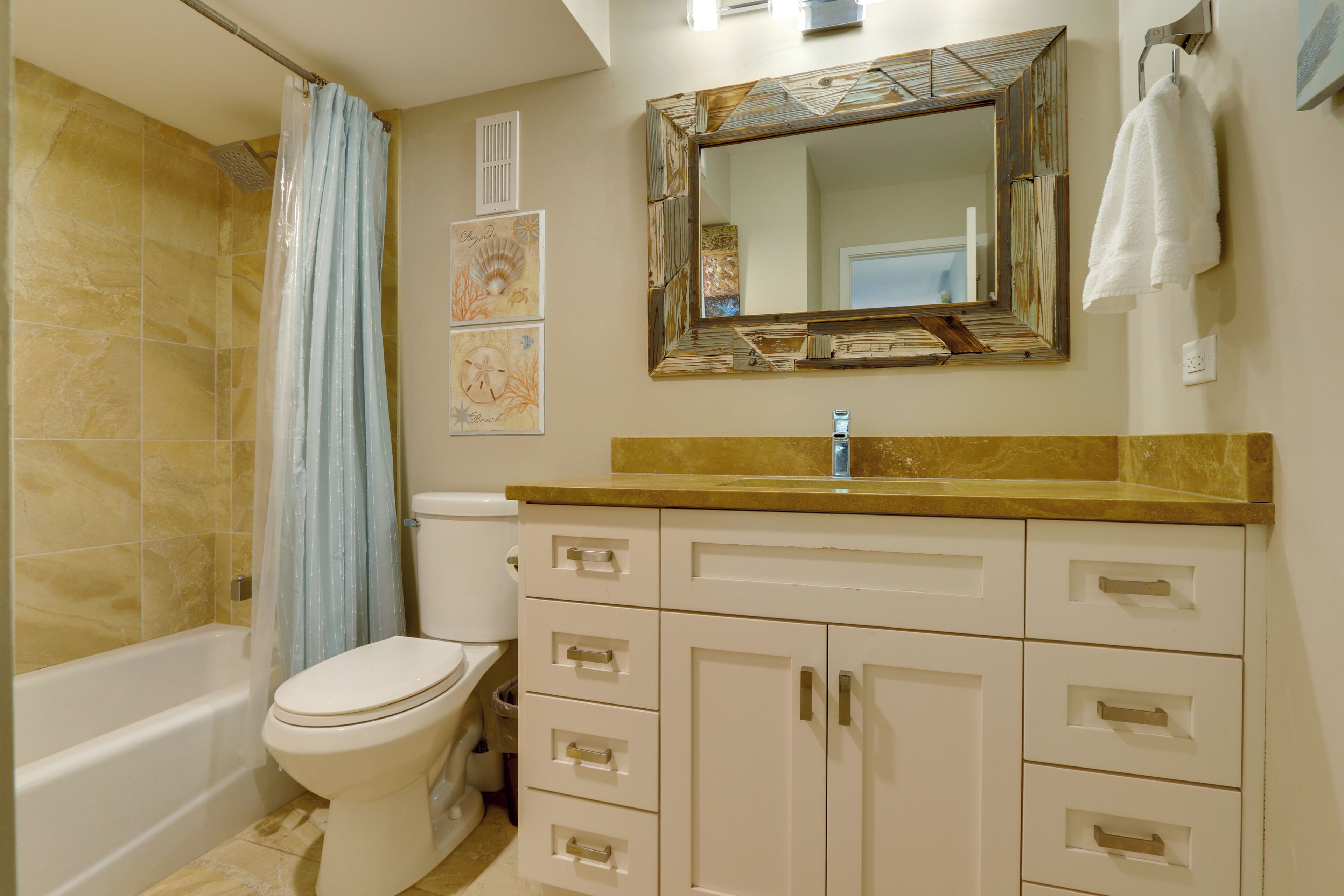 A bathroom with a bathtub, toilet, vanity with drawers, a mirror, and a shower curtain.