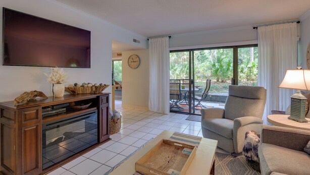 A living room with a flat-screen TV, a fireplace, a sofa, and a dining area with a table and chairs. - Serene Hilton Head Island Condo w/ Community Pool! (Hilton Head Island)