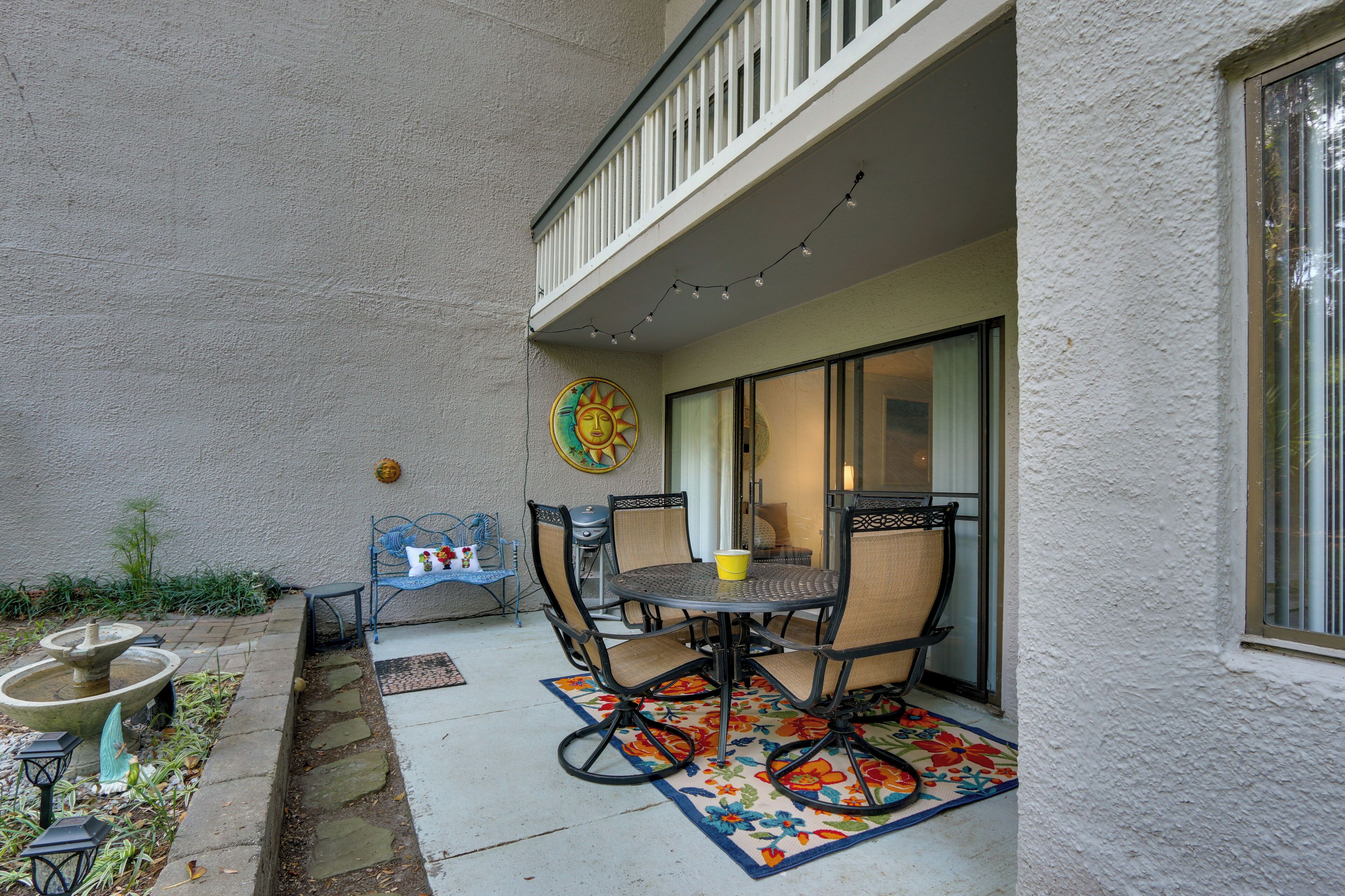 A patio with a table and chairs, a small fountain, and a decorative wall piece.