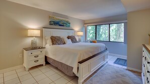 A bedroom with a large bed, bedside lamps, a nightstand, a dresser, and a window with a view of trees. - Serene Hilton Head Island Condo w/ Community Pool! (Hilton Head Island)