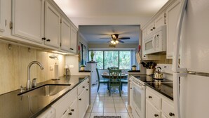 A kitchen with white cabinets, a black countertop, a sink, a ceiling fan, and a window with a view of trees. - Serene Hilton Head Island Condo w/ Community Pool! (Hilton Head Island)