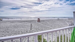 Une vue sur la plage depuis un balcon, avec une tour de surveillance des sauveteurs, une plage de sable et l’océan.