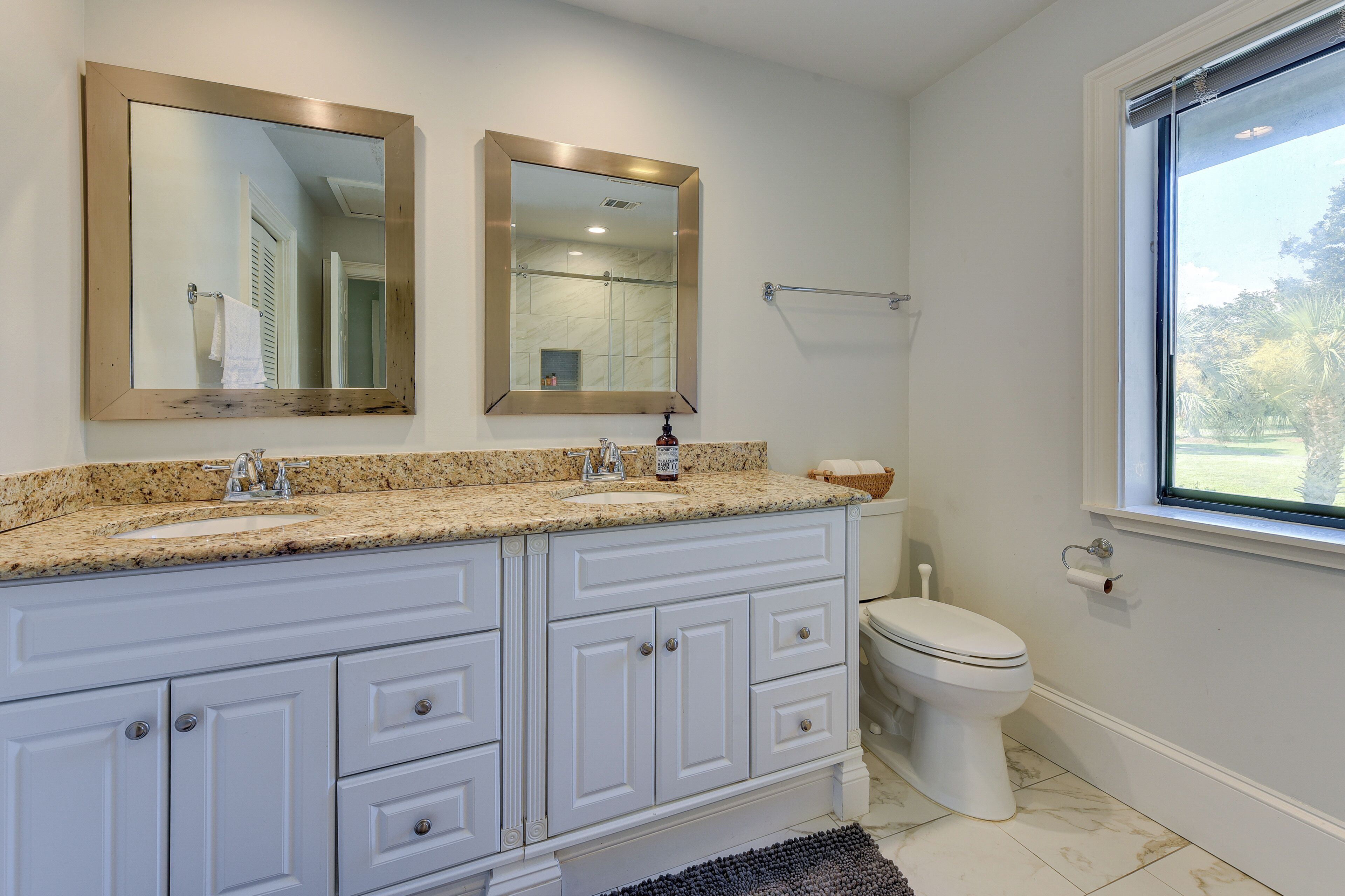 A bathroom with two sinks, a toilet, and a window.