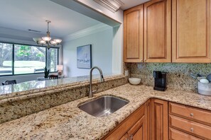 A kitchen with granite countertops, wooden cabinets, a stainless steel sink, a coffee maker, and a view of the outdoors. - Palmetto Dunes Golf Getaway: Pool + Beach Access! (Hilton Head Island)