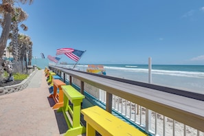 A beachside walkway with colorful benches, a railing, and American flags. - Daytona Beach Studio w/ Ocean View + Amenities! (Daytona Beach)