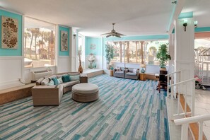 A spacious living room with a large window, a ceiling fan, and a view of palm trees. - Daytona Beach Studio w/ Ocean View + Amenities! (Daytona Beach)