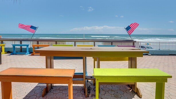A beachside area with wooden tables and benches, two American flags, and a view of the ocean. - Daytona Beach Studio w/ Ocean View + Amenities! (Daytona Beach)