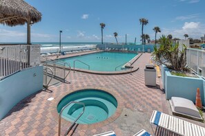 A pool area with a view of the ocean, a thatched roof structure, and lounge chairs. - Daytona Beach Studio w/ Ocean View + Amenities! (Daytona Beach)