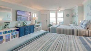 A bedroom with two beds, a desk, a chair, and a window with a view. - Daytona Beach Studio w/ Ocean View + Amenities! (Daytona Beach)