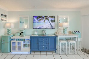 A room with a blue cabinet, a white desk, a TV, and a beach-themed painting. - Daytona Beach Studio w/ Ocean View + Amenities! (Daytona Beach)