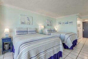 A room with two beds, a nightstand with a lamp, and wall art. - Daytona Beach Studio w/ Ocean View + Amenities! (Daytona Beach)