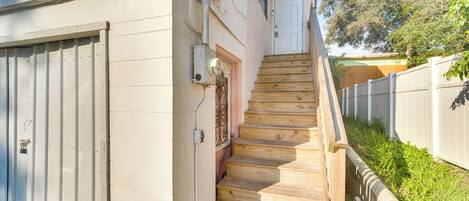 Una escalera de madera que conduce a una puerta blanca, un portón metálico y una valla blanca.