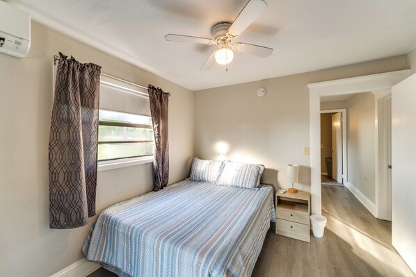 A bedroom with a bed, curtains, a ceiling fan, a bedside table, and a nightstand.