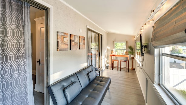 A modern interior with a black leather sofa, a dining area with a table and chairs, and artwork on the walls. - Quiet Apt: Walk to Daytona Beach + Water Park! (Daytona Beach)