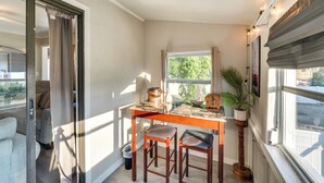 A compact kitchen with a wooden table, two stools, a potted plant, and a window with curtains. - Quiet Apt: Walk to Daytona Beach + Water Park! (Daytona Beach)