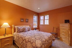 Une chambre à coucher avec un lit, deux lampes de chevet, une commode, une chaise et une fenêtre avec des rideaux.