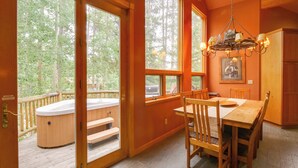 A wooden interior with a dining table and chairs, a hot tub outside, and large windows offering a view of trees. - Hot Tub & Ski Shuttle: Rustic Breckenridge Retreat (Breckenridge)
