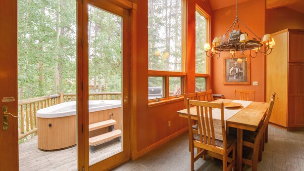 A wooden interior with a dining table and chairs, a hot tub outside, and large windows offering a view of trees. - Hot Tub & Ski Shuttle: Rustic Breckenridge Retreat (Breckenridge)