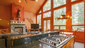 A kitchen with a stone fireplace, a large island with a gas stove, and a mounted deer head. - Hot Tub & Ski Shuttle: Rustic Breckenridge Retreat (Breckenridge)