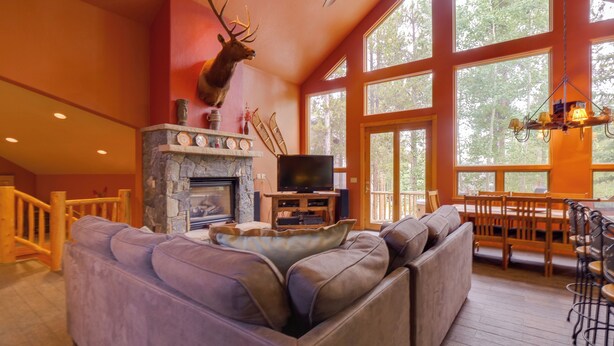 A spacious living room with a stone fireplace, a mounted deer head, a large window, and a cozy seating area. - Hot Tub & Ski Shuttle: Rustic Breckenridge Retreat (Breckenridge)