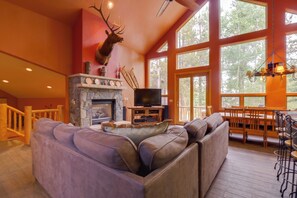 A spacious living room with a stone fireplace, a mounted deer head, a large window, and a cozy seating area. - Hot Tub & Ski Shuttle: Rustic Breckenridge Retreat (Breckenridge)