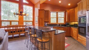 A spacious kitchen with wooden cabinets, a large island with bar stools, and a view of the forest through large windows. - Hot Tub & Ski Shuttle: Rustic Breckenridge Retreat (Breckenridge)