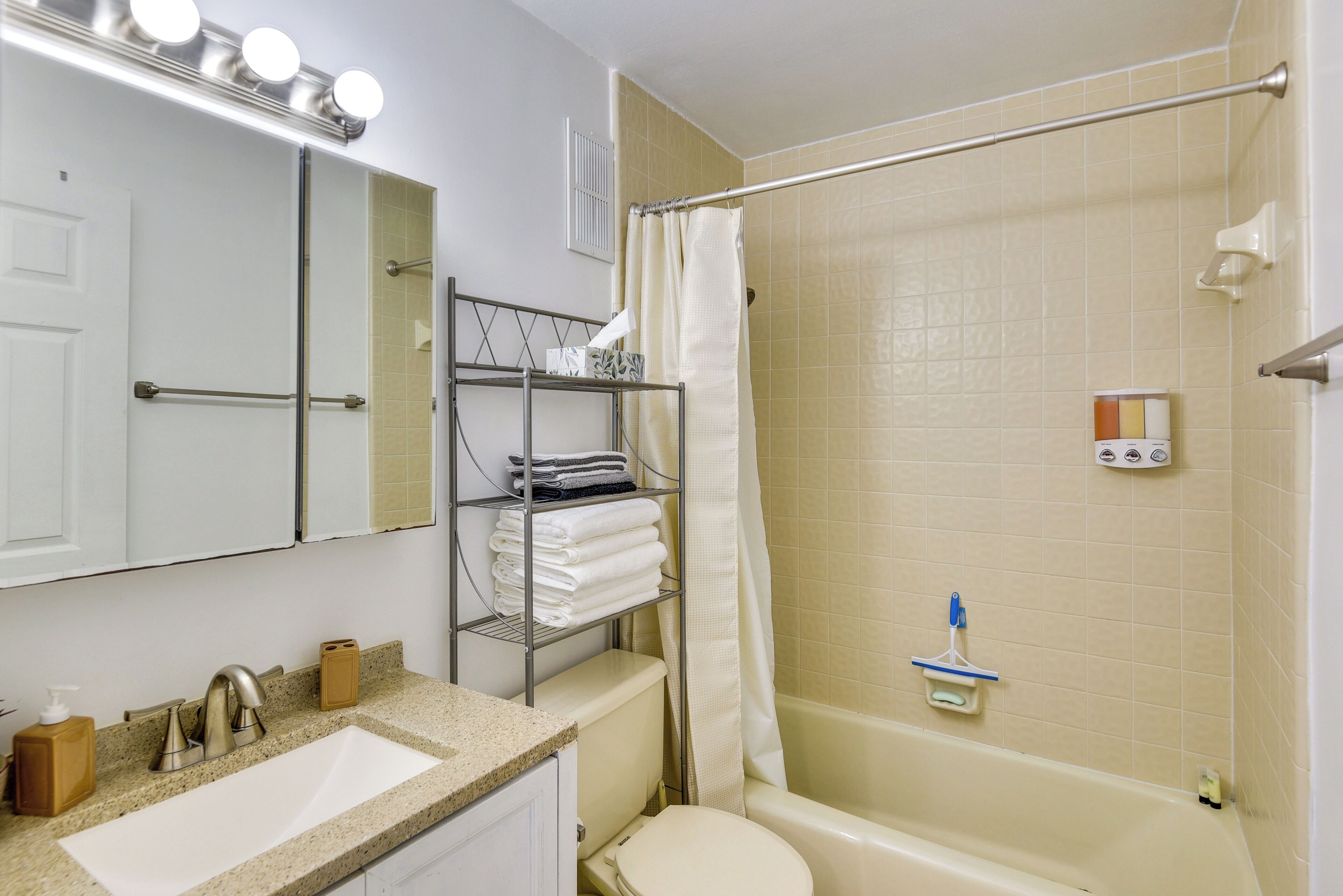 Ein Badezimmer mit Waschbecken, Toilette und Badewanne. Ein Regal bietet Handtücher und Toilettenartikel.