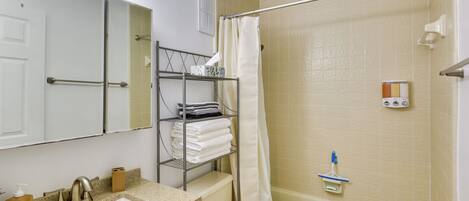 A bathroom with a sink, toilet, and bathtub. There is a shelf with towels and toiletries.