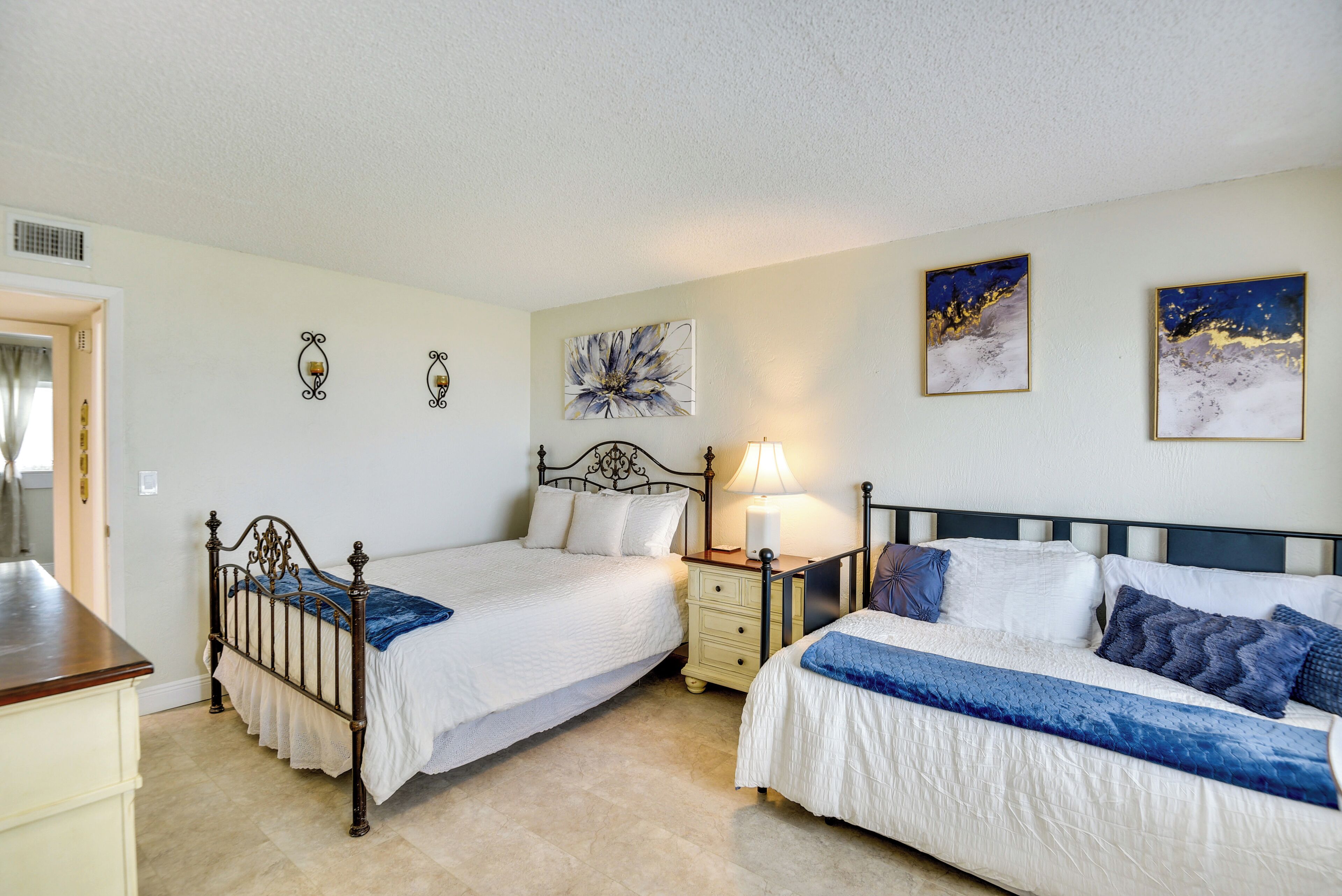 A bedroom with two beds, a nightstand, a lamp, and wall art.