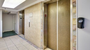 A hallway with an elevator, a door with a number plate, and a wall-mounted device. - Daytona Beach Vacation Rental w/ Pool Access (Daytona Beach Shores)