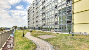 A modern building with a glass facade, a paved walkway, and a grassy area. - Daytona Beach Vacation Rental w/ Pool Access (Daytona Beach Shores)
