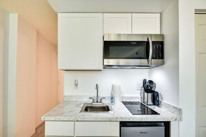 Een kleine keuken met witte kastjes, een stalen magnetron, een spoelbak en een vaatwasser.